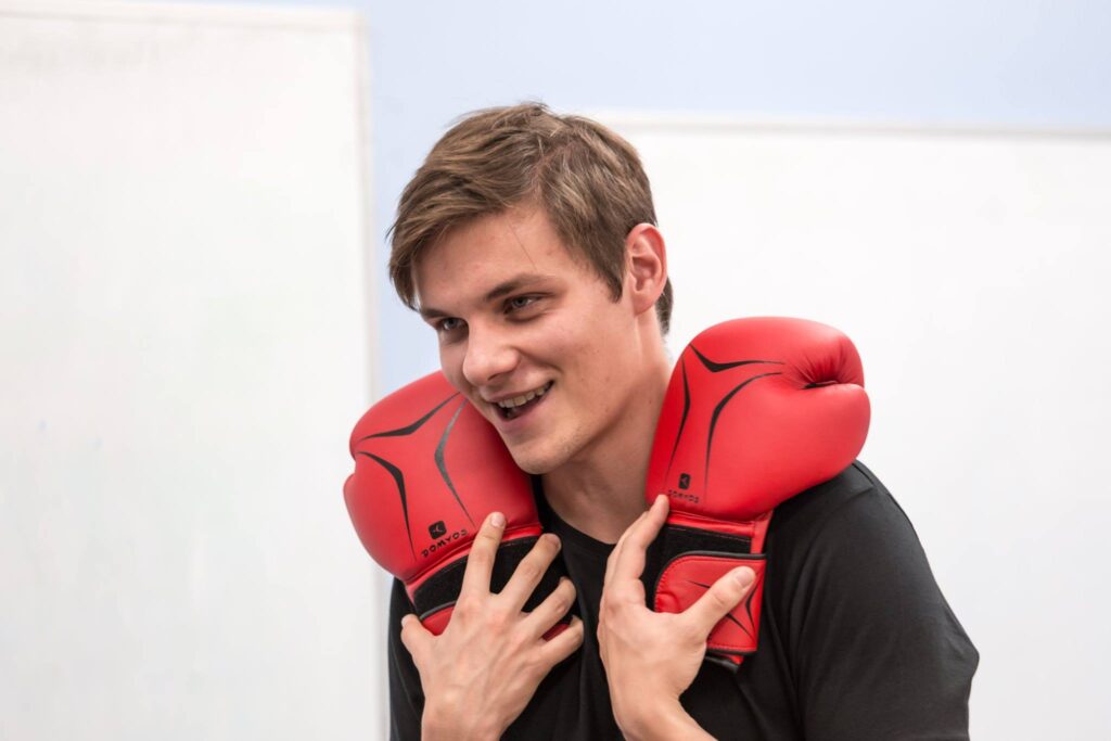 Zdjęcie ze spektaklu Trik Patryka. Aktor trzyma rękawice bokserskie i przykłada je do ramion, otwiera usta.