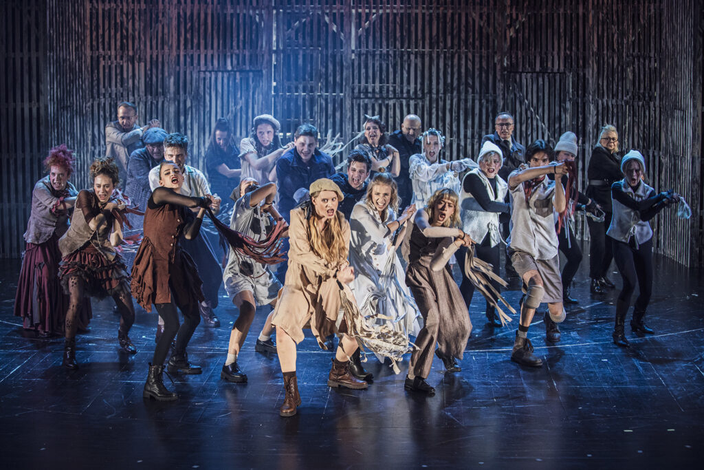 Zdjęcie ze spektaklu Folwark zwierzęcy. Scena zbiorowa. Aktorzy i aktorki są w dynamicznych pozach tańczą. Ich kostiumy symbolizują różne zwierzęta.