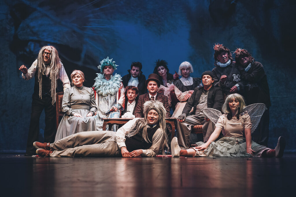 Zdjęcie ze spektaklu Doktor Dolittle. Zdjęcie grupowe aktorów i aktorek występujących w spektaklu. Większość ma peruki i rekwizyty/atrybuty symbolizujące zwierzęta.