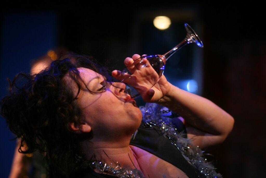 Zdjęcie ze spektaklu Wszystko o kobietach. Zbliżenie. Aktorka pije z kieliszka.