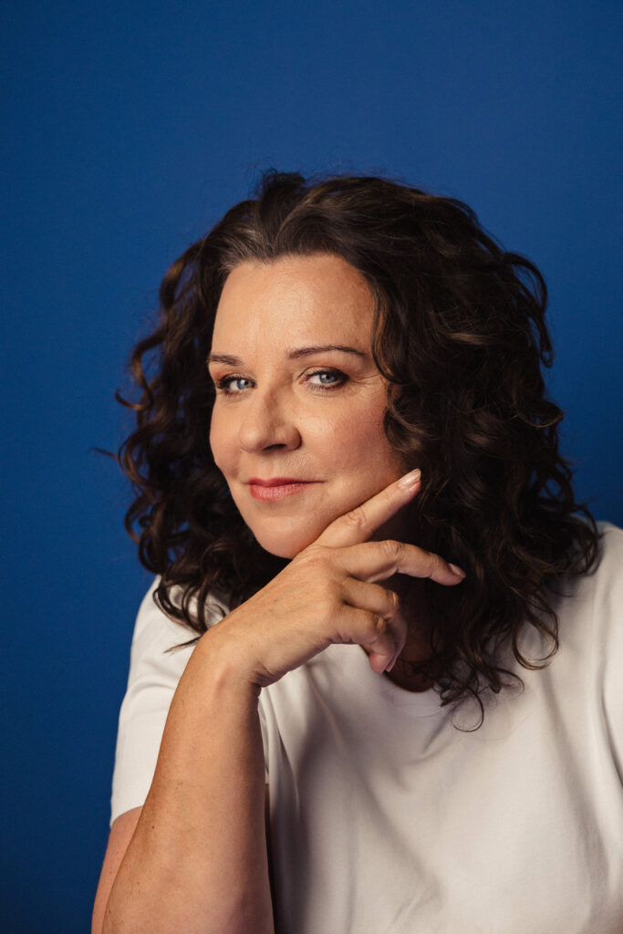 Zdjęcie portretowe aktorki Beaty Schimscheiner, delikatny uśmiech, twarz podparta ręką.