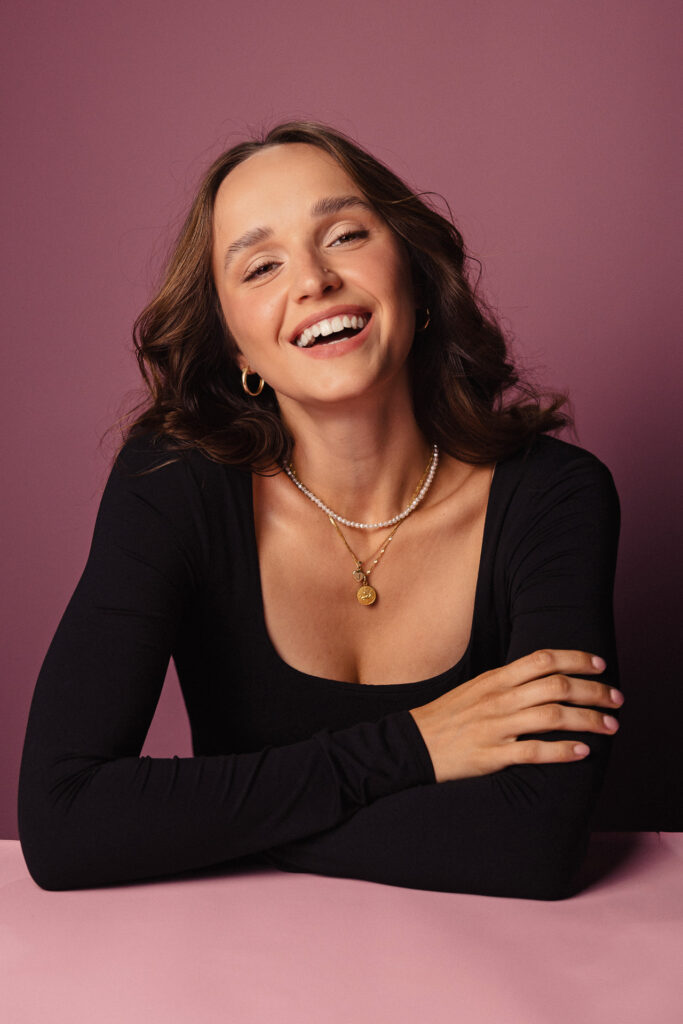 Zdjęcie portretowe aktorki Justyny Litwic, szeroki uśmiech, ręce skrzyżowane przed sobą.