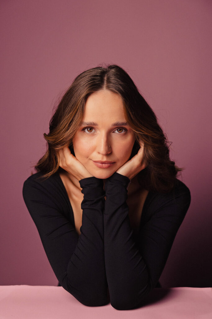 Zdjęcie profilowe portretowe aktorki Justyny Litwic, delikatny uśmiech, ręce podpierają brodę.