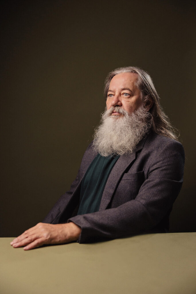 Zdjęcie półprofil portretowe aktora Kajetana Wolniewicza, poważna twarz, ręce przed sobą.