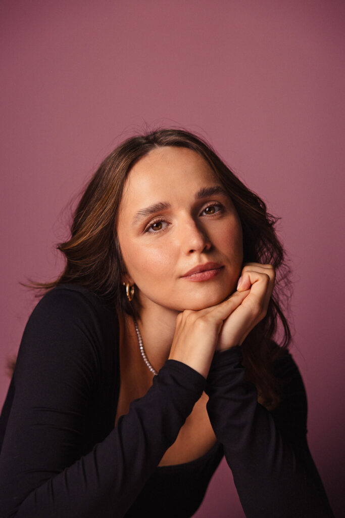 Zdjęcie portretowe aktorki Justyny Litwic, delikatny uśmiech, ręce podpierają brodę.