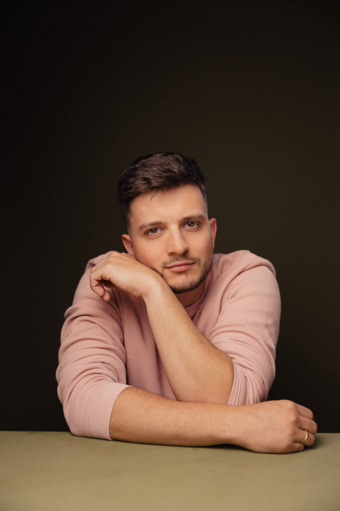 Zdjęcie portretowe aktora Roberta Ratusznego, poważna twarz, ręka podpiera twarz.