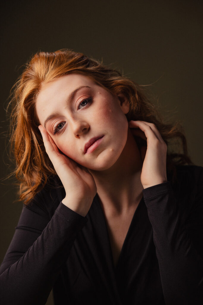 Zdjęcie portretowe aktorki Doroty Goljasz, neutralna twarz pochylona na bok, ręce dotykają twarzy.