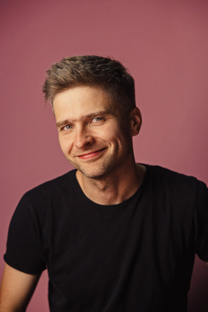 Zdjęcie portretowe aktora Karola Polaka, szeroki uśmiech, bliski kadr.