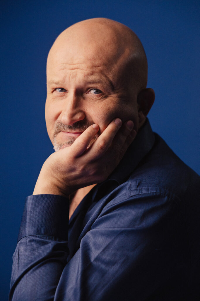 Zdjęcie profilowe portretowe aktora Jana Nosala, lekki uśmiech, dłoń podpiera brodę.