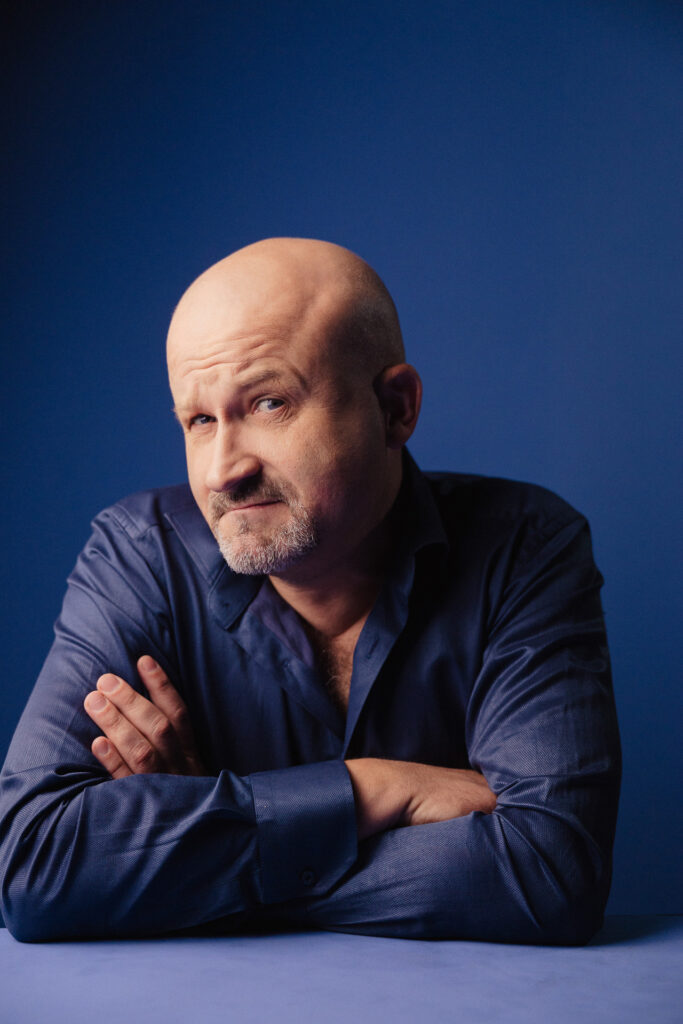 Zdjęcie portretowe aktora Jana Nosala, poważna twarz przechylona lekko do profilu, ręce skrzyżowane przed sobą.