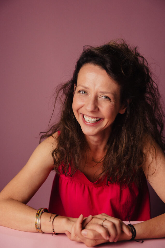 Zdjęcie portretowe aktorki Iwony Sitkowskiej, szeroki uśmiech, ręce skrzyżowane przed sobą.