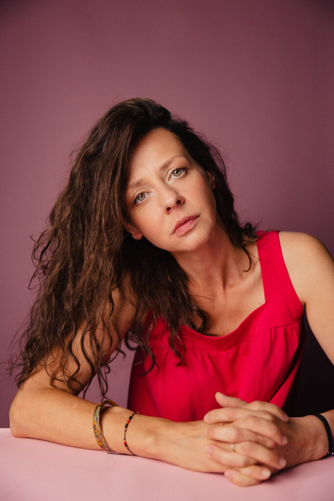 Zdjęcie portretowe aktorki Iwony Sitkowskiej, przechylona głowa, twarz neutralna, ręce skrzyżowane przed sobą.