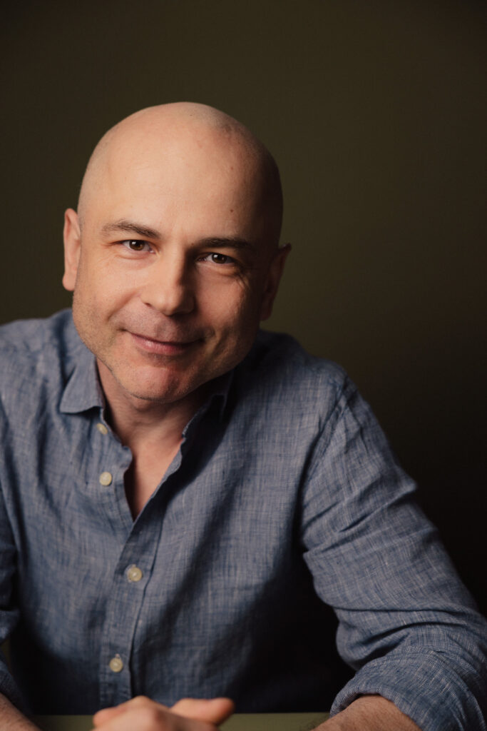 Zdjęcie portretowe aktora Macieja Namysło, lekki uśmiech, bliski kadr.