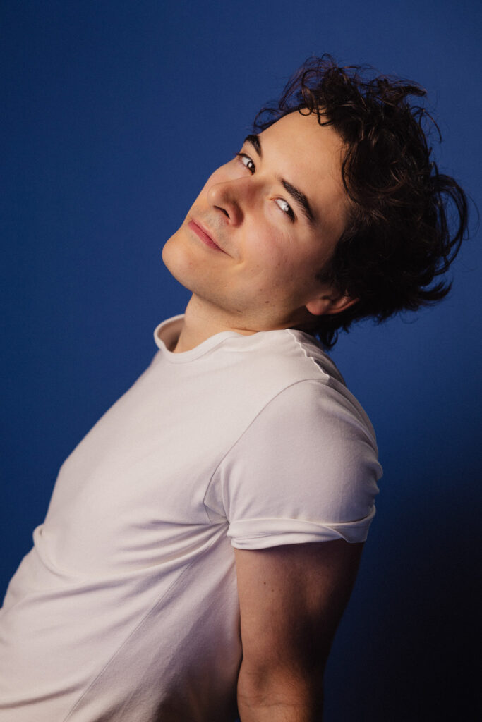 Zdjęcie portretowe profilowe aktora Antoniego Włosowicza, delikatny uśmiech, sylwetka wygięta oparta na rękach