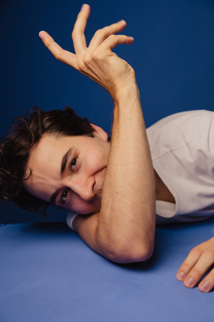 Zdjęcie portretowe aktora Antoniego Włosowicza, ręka w górze zasłania częściowo twarz, sylwetka leżąca.