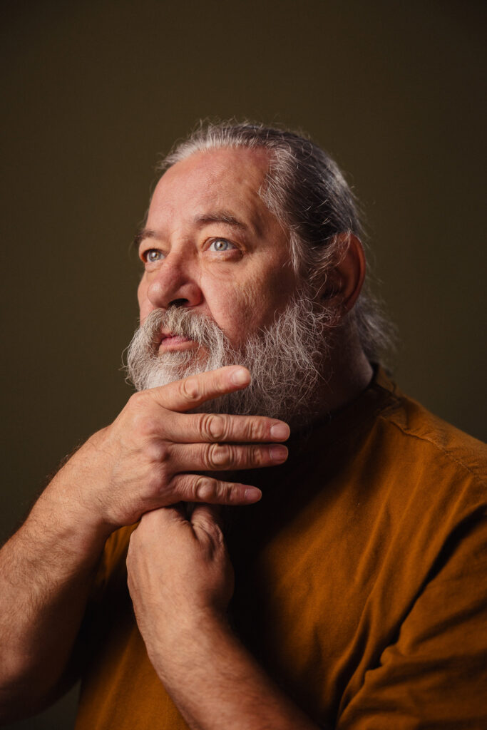 Zdjęcie półprofil portretowe aktora Kajetana Wolniewicza, poważna twarz, bliski kadr, ręce dotykają brody