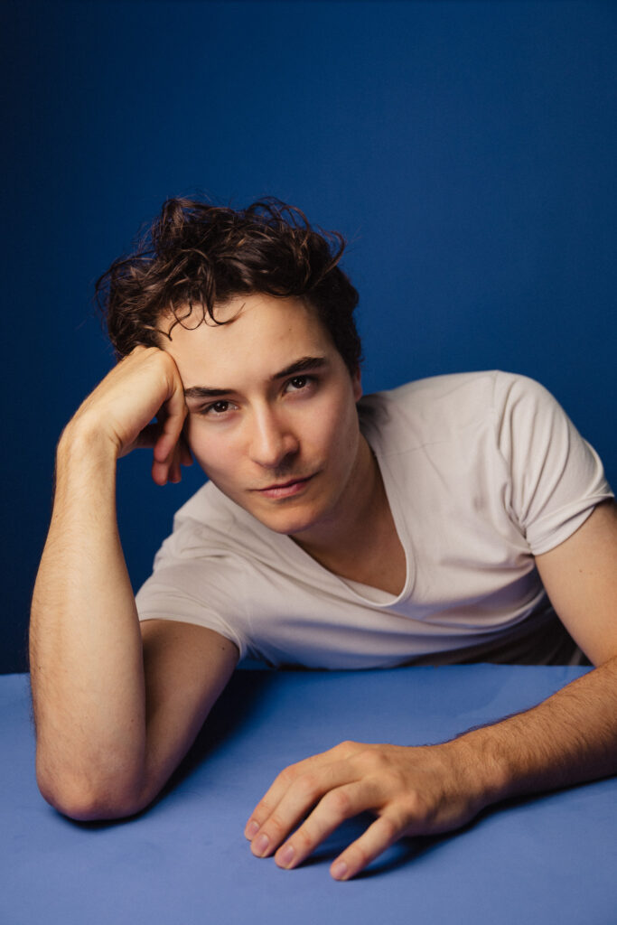 Zdjęcie portretowe aktora Antoniego Włosowicza, neutralna twarz, ręka podpiera czoło.