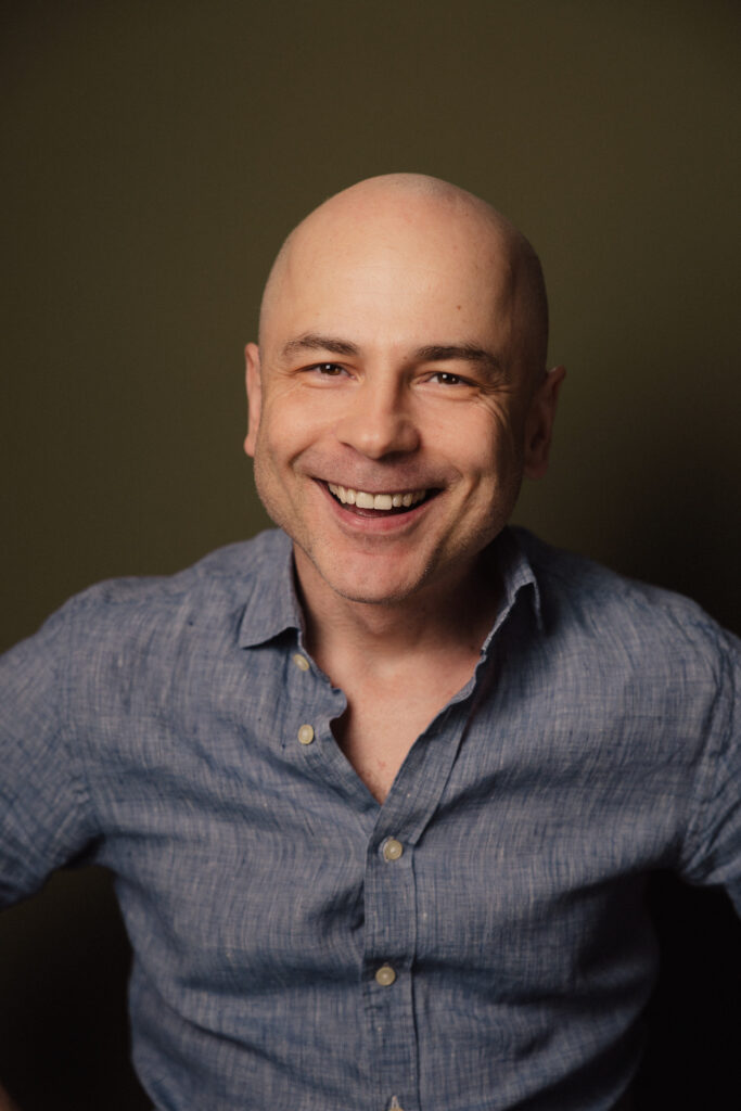 Zdjęcie portretowe aktora Macieja Namysło, szeroki uśmiech, bliski kadr.