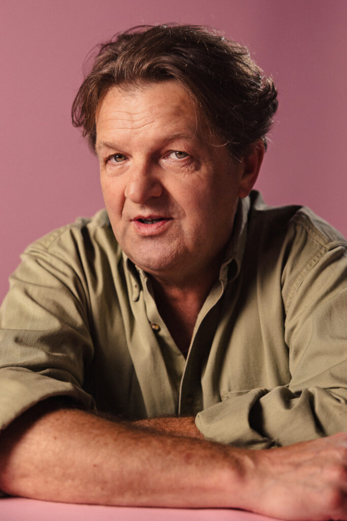 Zdjęcie portretowe aktora Jacka Wojciechowskiego, delikatny uśmiech, ręce skrzyżowane przed sobą.