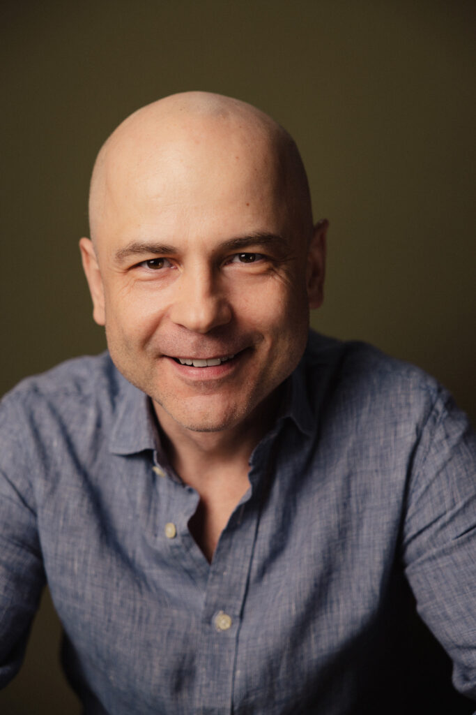 Zdjęcie portretowe aktora Macieja Namysło, lekki uśmiech, bliski kadr.