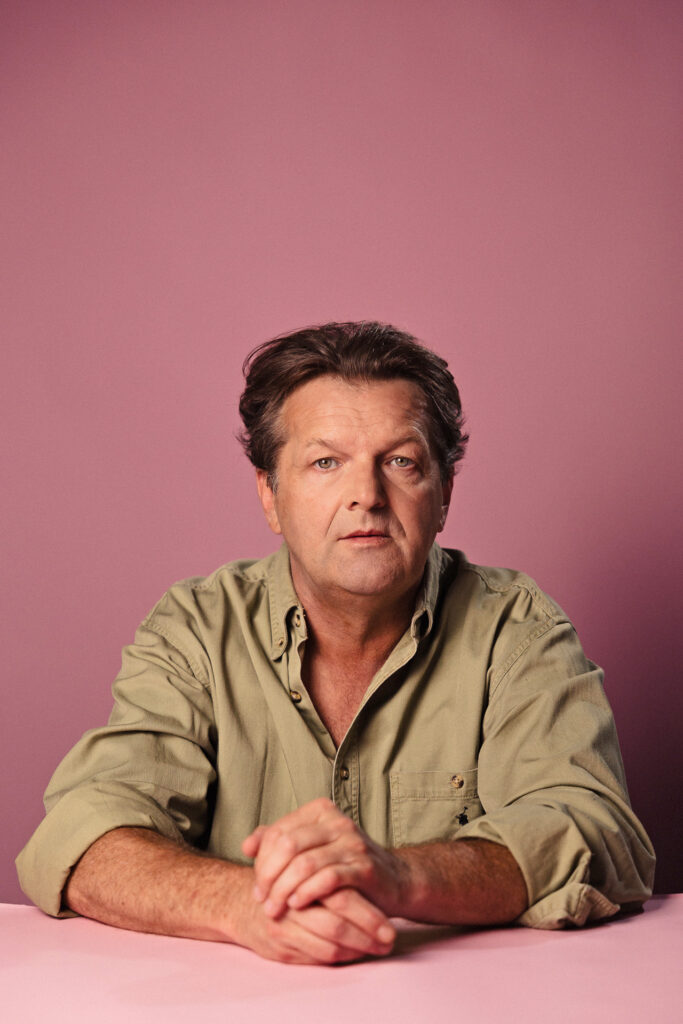 Zdjęcie portretowe aktora Jacka Wojciechowskiego, poważna twarz, ręce skrzyżowane przed sobą.