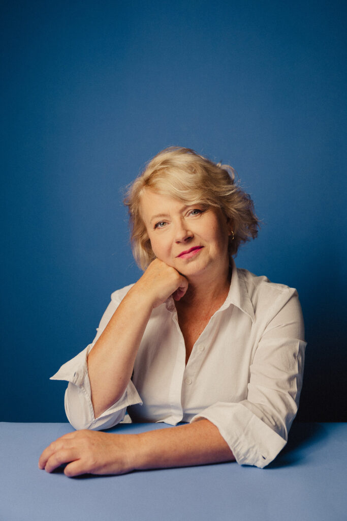 Zdjęcie portretowe aktorki Małgorzaty Kochan, lekki uśmiech, ręce skrzyżowane przed sobą jedna podpiera twarz.