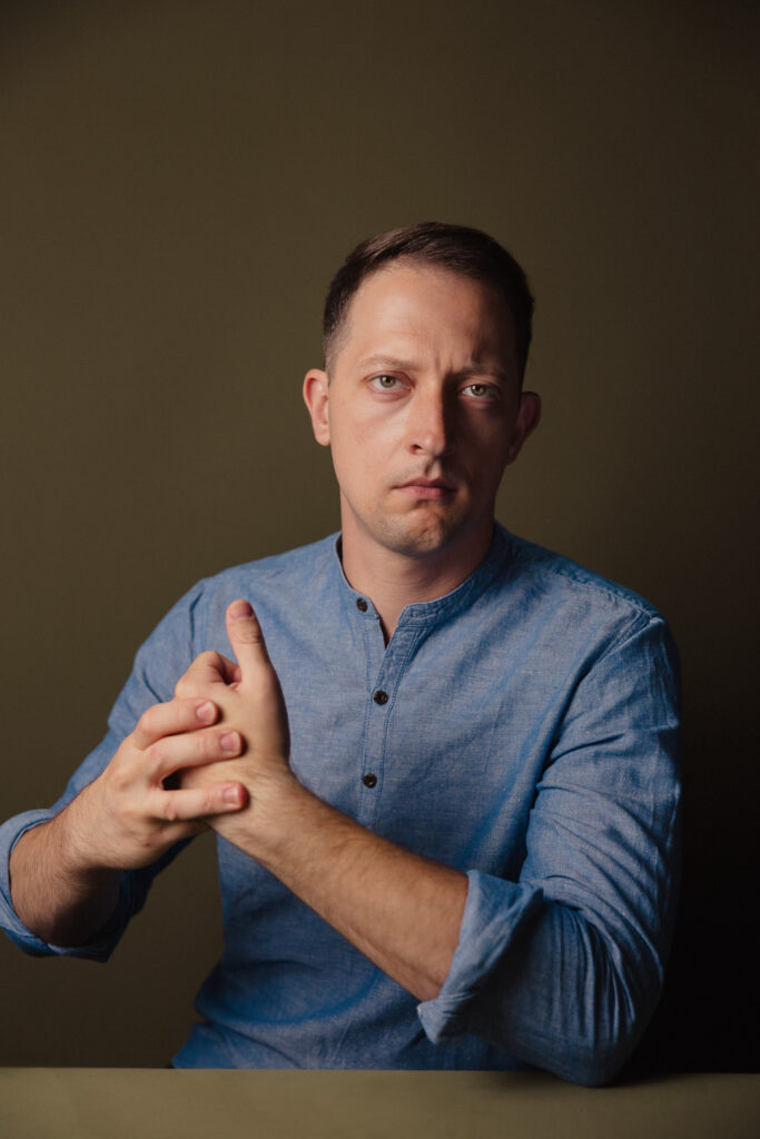 Zdjęcie profilowe portretowe aktora Wojciecha Lato, poważana twarz, ręce splecione przed sylwetką