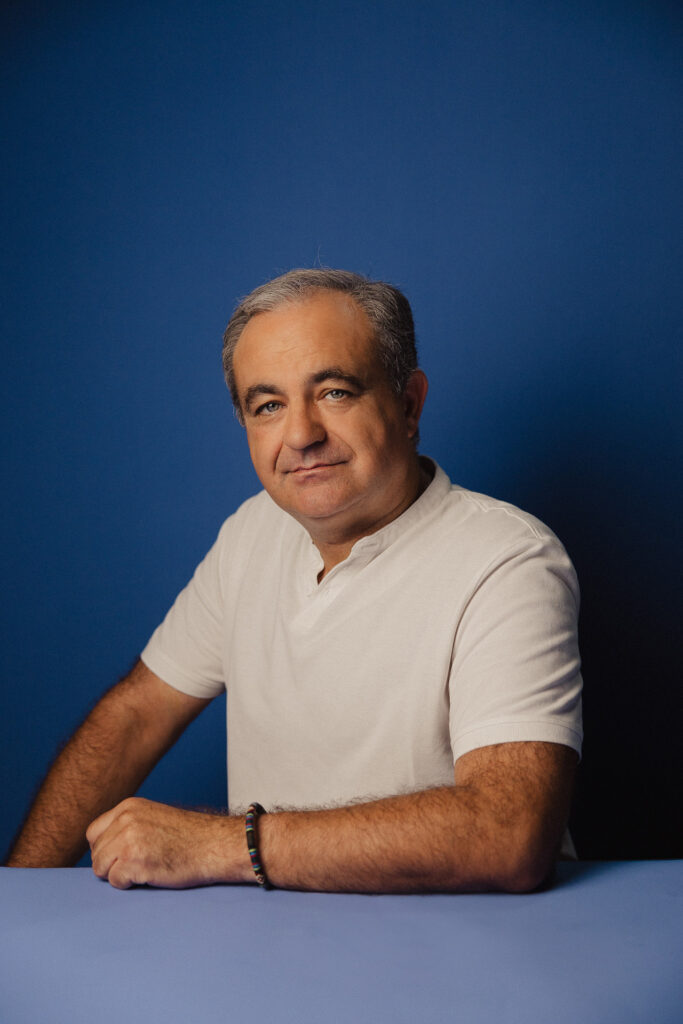 Zdjęcie profilowe portretowe aktora Tadeusza Łomnickiego, lekki uśmiech, ręce przed sobą.