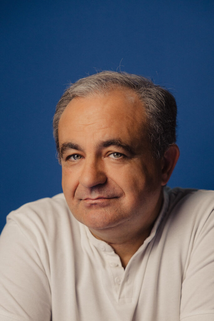 Zdjęcie półprofil profilowe portretowe aktora Tadeusza Łomnickiego, lekki uśmiech, bliski kadr.