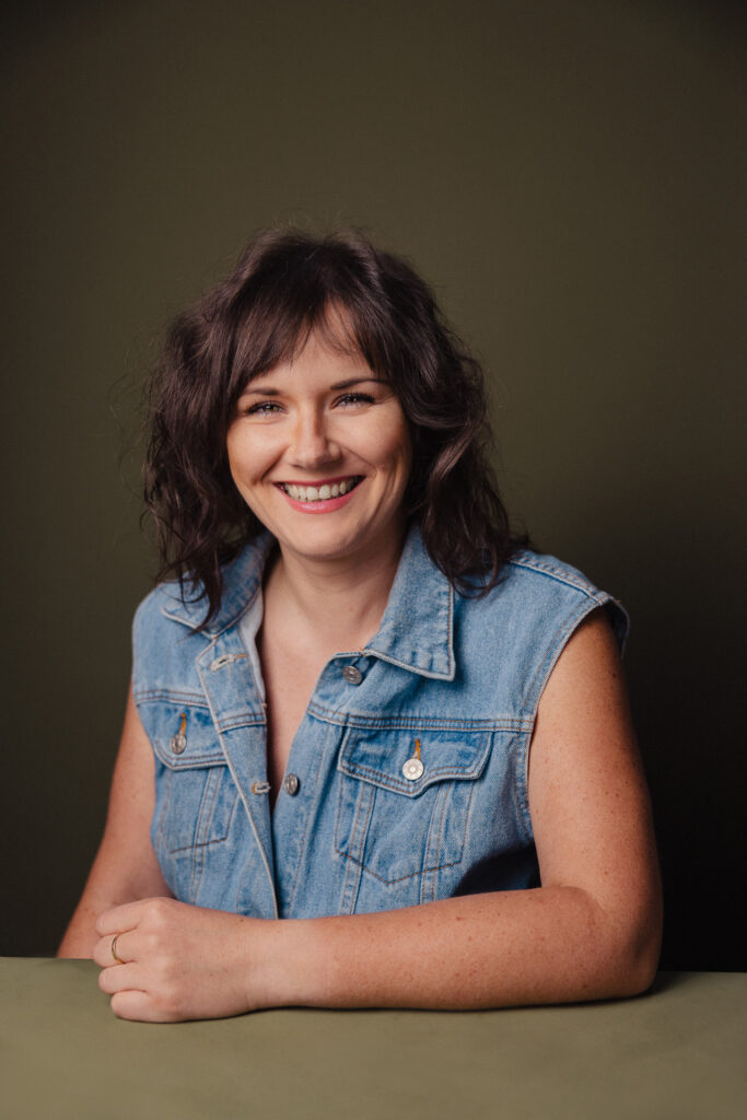 Zdjęcie półprofil portretowe aktorki Weroniki Kowalskiej, szeroki uśmiech, ręce przed sobą.