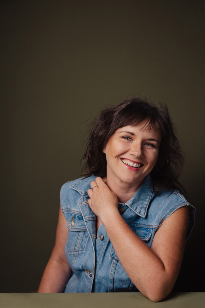 Zdjęcie półprofil portretowe aktorki Weroniki Kowalskiej, lekki uśmiech, ręce przy szyi.