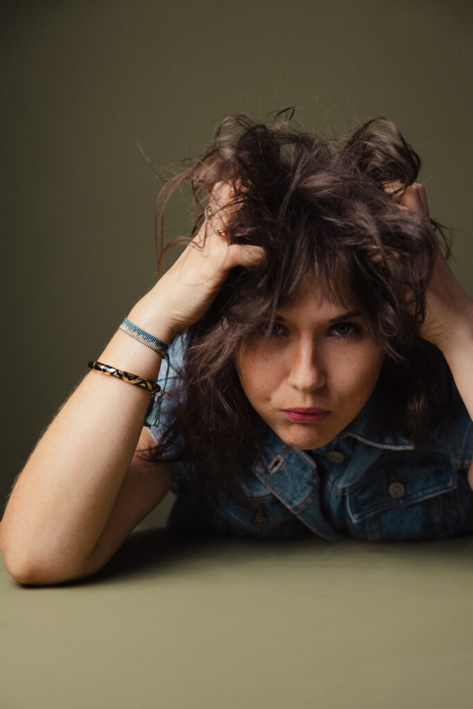 Zdjęcie portretowe aktorki Weroniki Kowalskiej, dynamiczne, poważna twarz, bliski kadr, ręce we włosach.