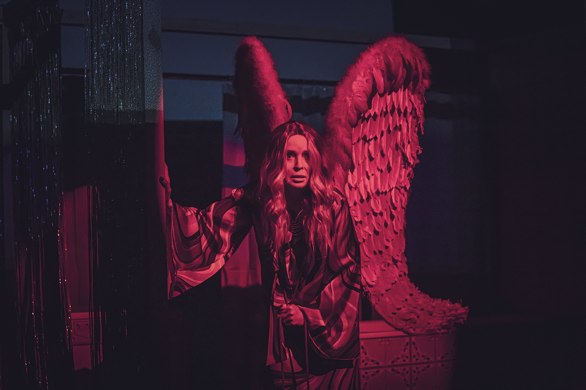 Zdjęcie ze spektaklu Aktorzy prowincjonalni. Zdjęcie zabarwione na czerwono. Aktorka ma na plecach duże skrzydła z piór.