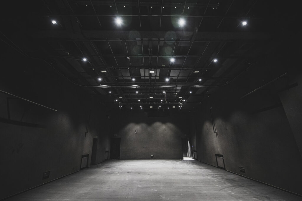 Scena Kameralna w budynku Teatralnego Instytutu Młodych. Scena jest pusta z zdemontowaną widownią. Ściany i podłoga w czarnym kolorze, u góry punktowe oświetlenie.