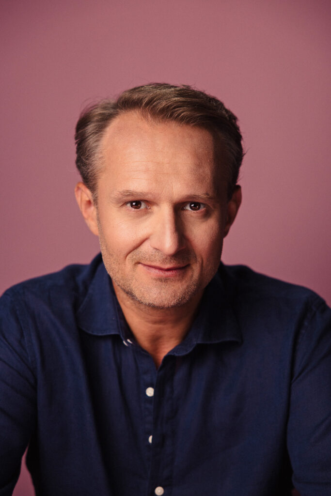 Zdjęcie półprofil portretowe aktora Pawła Kumięgi, poważna twarz, bliski kadr.