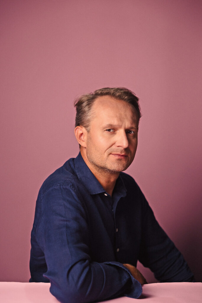 Zdjęcie półprofil portretowe aktora Pawła Kumięgi, poważna twarz, bliski kadr.