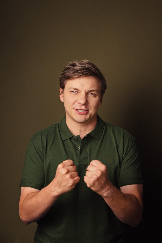 Zdjęcie portretowe aktora Ryszarda Starosty, dynamiczne, poważna twarz, bliski kadr, ręce zaciśnięte w pięści przed sobą.