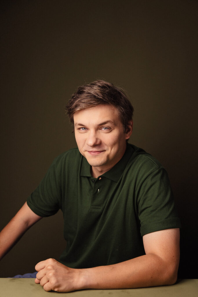 Zdjęcie portretowe aktora Ryszarda Starosty, lekki uśmiech, bliski kadr, ręce przed sobą.