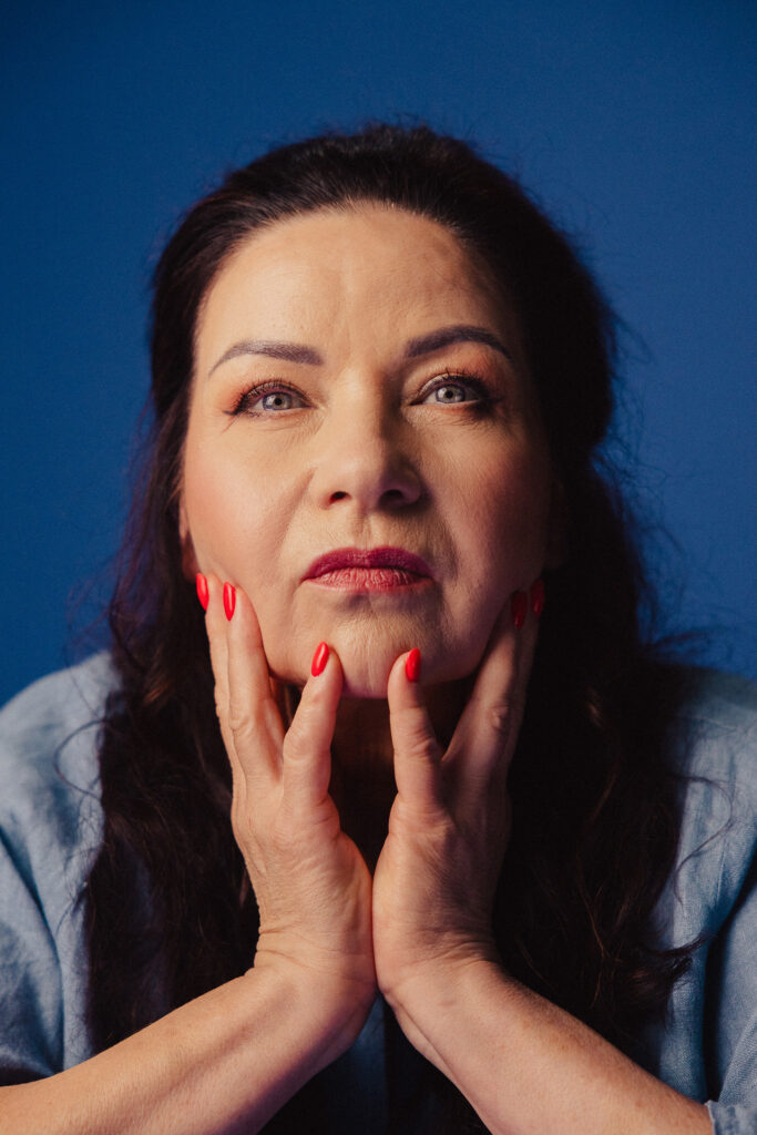 Zdjęcie portretowe aktorki Małgorzaty Krzysica, poważna twarz, ręce dotykają twarzy, bliski kadr.