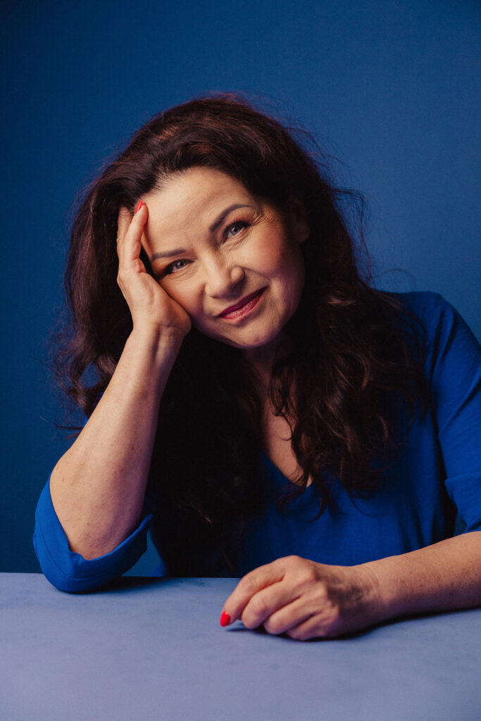 Zdjęcie portretowe aktorki Małgorzaty Krzysica, lekki uśmiech, ręce dotykają włosów.