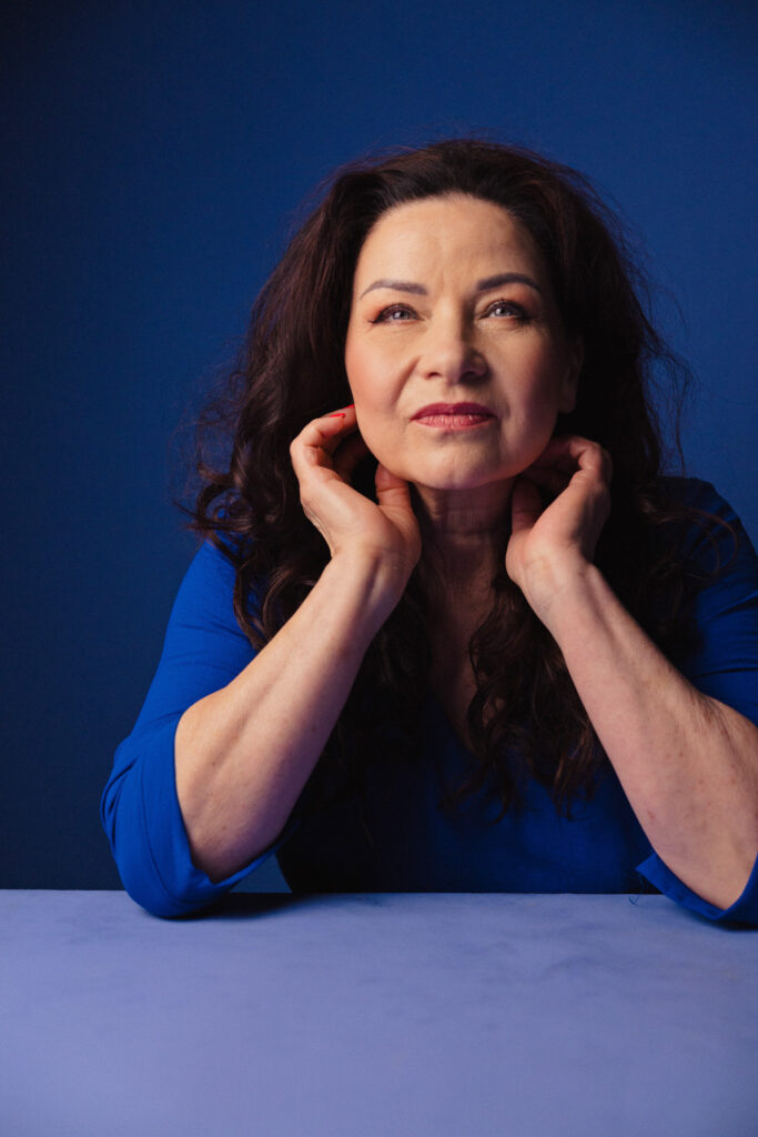 Zdjęcie portretowe aktorki Małgorzaty Krzysica, poważna twarz, ręce dotykają uszu.