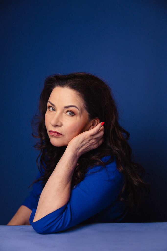 Zdjęcie półprofil portretowe aktorki Małgorzaty Krzysica, poważna twarz, ręce dotykają włosów.