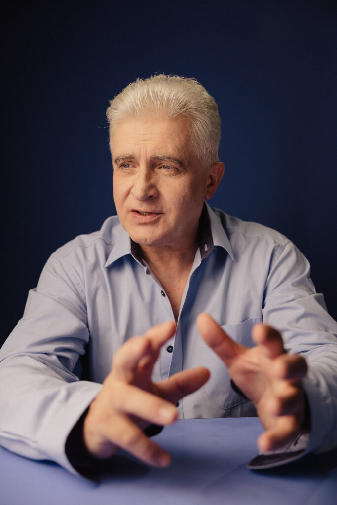 Zdjęcie portretowe aktora Piotra Piechy, poważna twarz, ręce dynamiczne wyciągnięte przed sylwetką.