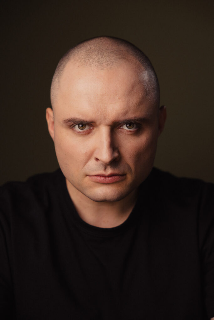 Zdjęcie portretowe aktora Patryka Palusińskiego, poważna twarz, bliski kadr.