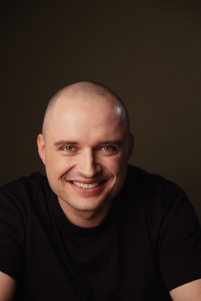 Zdjęcie portretowe aktora Patryka Palusińskiego, szeroki uśmiech, bliski kadr.