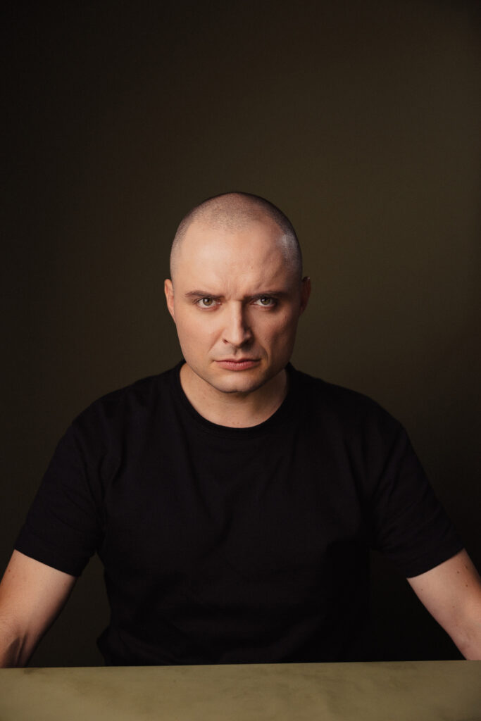 Zdjęcie portretowe aktora Patryka Palusińskiego, poważna twarz, bliski kadr.