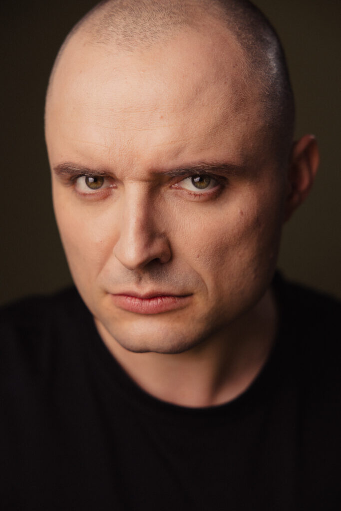 Zdjęcie portretowe aktora Patryka Palusińskiego, poważna twarz, bliski kadr.