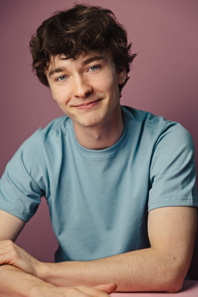 Zdjęcie portretowe aktora Marcina Mazurka, lekki uśmiech, bliski kadr, ręce skrzyżowane przed sobą.