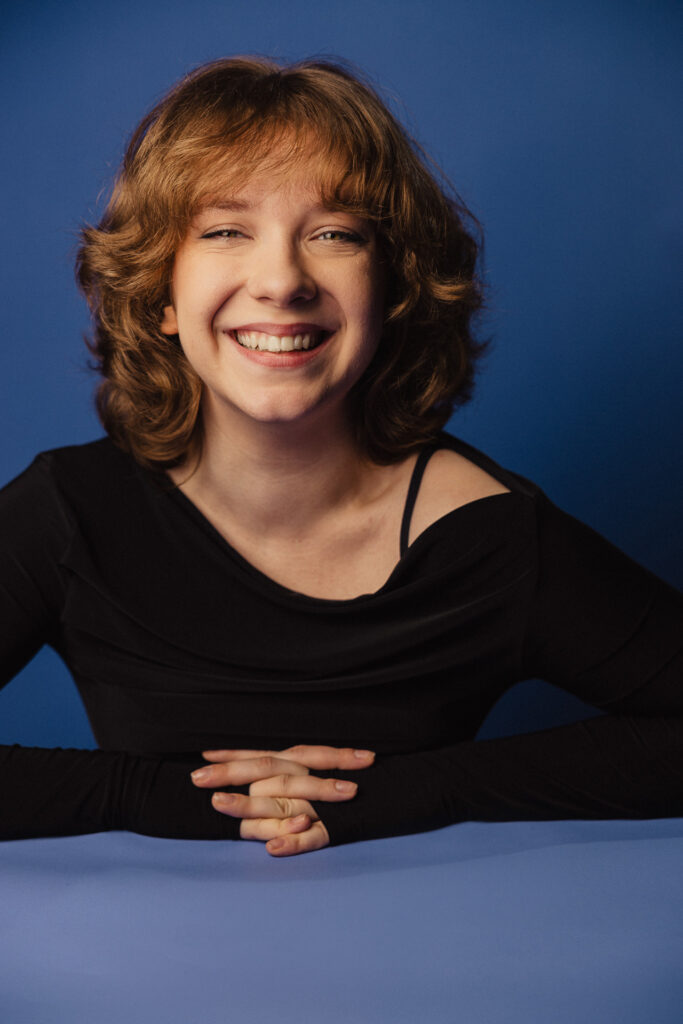 Zdjęcie portretowe aktorki Michaliny Dworzaczek, szeroki uśmiech, ręce splecione przed sobą.