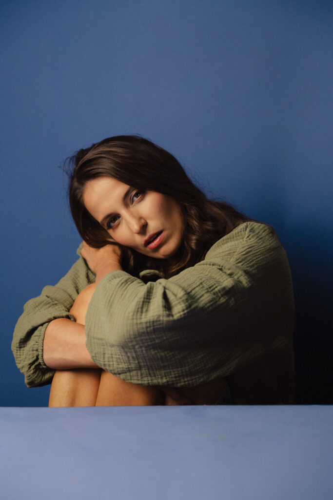 Zdjęcie portretowe aktorki Roksany Lewak, poważna twarz, bliski kadr.ręce otulają sylwetkę.